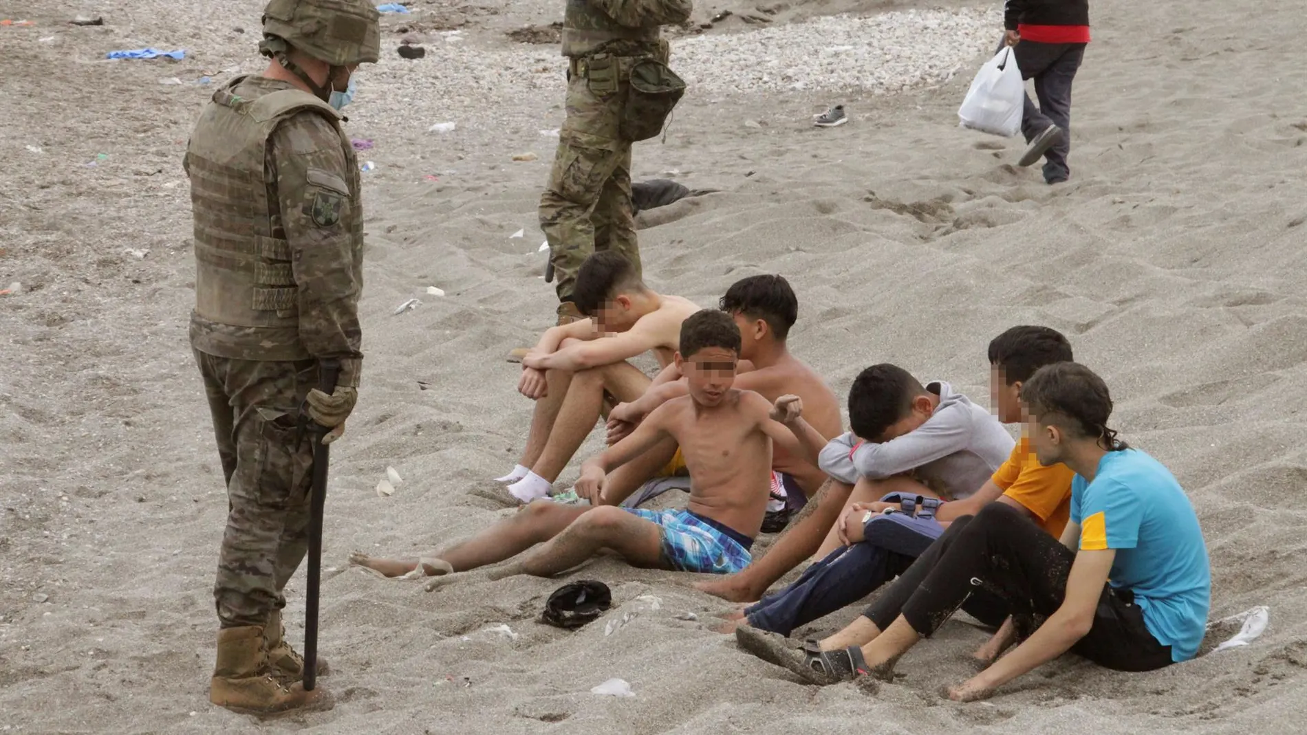 Miembros del Ejército de Tierra vigilan a un grupo de inmigrantes menores que han logrado cruzar uno de los espigones fronterizos de Ceuta 