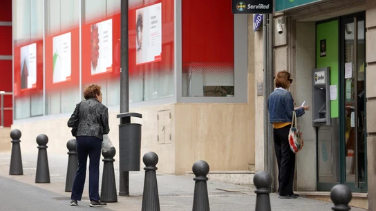 Una mujer saca dinero en un cajero automático de un banco mientras otra espera Una mujer saca dinero en un cajero automático mientras otra espera