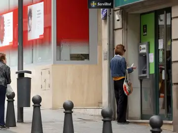 Una mujer saca dinero en un cajero automático de un banco mientras otra espera