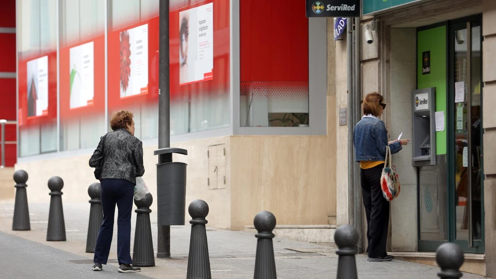 Una mujer saca dinero en un cajero automático mientras otra espera