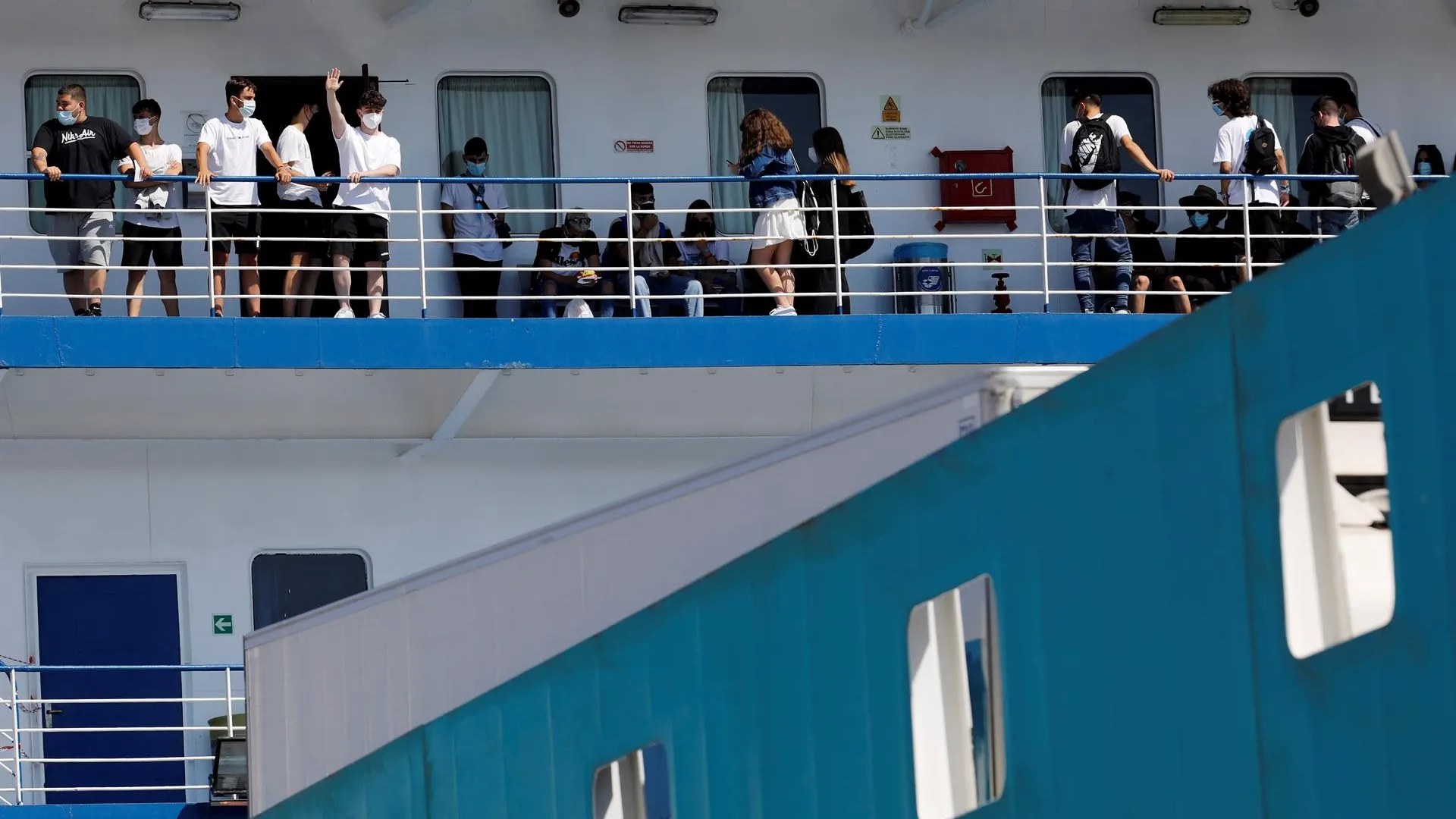  Varias personas saludan desde el ferry en el que viajan 118 estudiantes que habían sido confinados en un hotel de Mallorca tras el macrobrote.