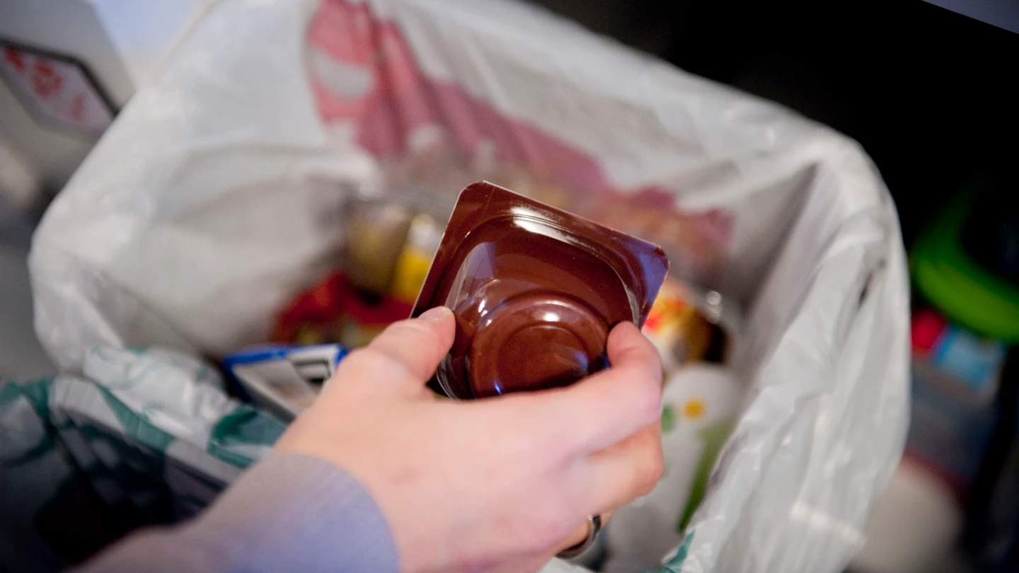 Una persona echa un envase de yogurt a un cubo destinado a ello en su hogar Una persona echa un envase de yogurt a un cubo destinado a ello en su hogar