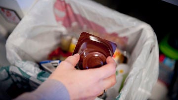 Una persona echa un envase de yogurt a un cubo destinado a ello en su hogar