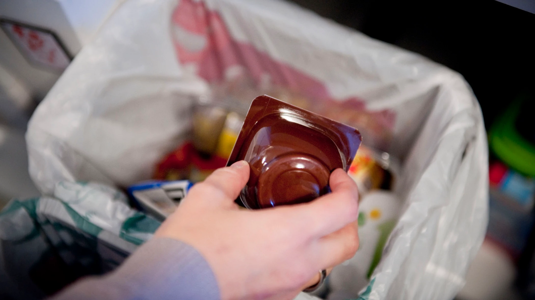 Una persona echa un envase de yogurt a un cubo destinado a ello en su hogar