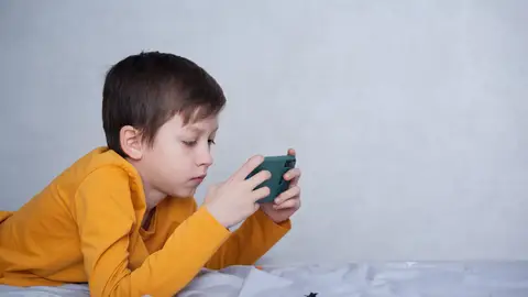 Un niño tumbado juega a un videojuego en su móvil