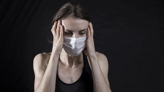Persona con mascarilla y un fuerte dolor de cabeza Persona con mascarilla y un fuerte dolor de cabeza
