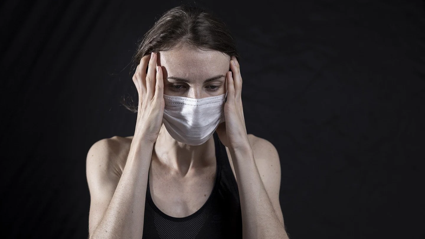 Persona con mascarilla y un fuerte dolor de cabeza Persona con mascarilla y un fuerte dolor de cabeza