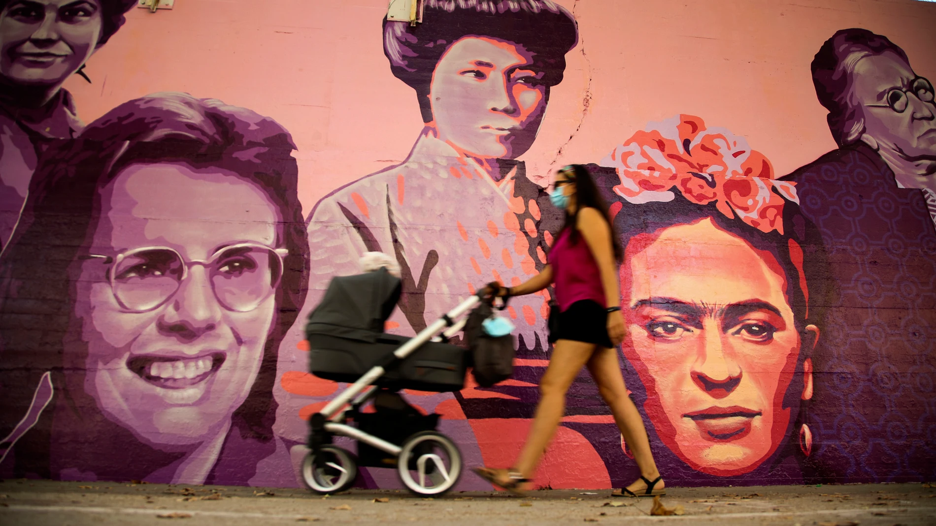 Una mujer camina junto al mural de las mujeres del barrio de Ciudad Lineal en Madrid