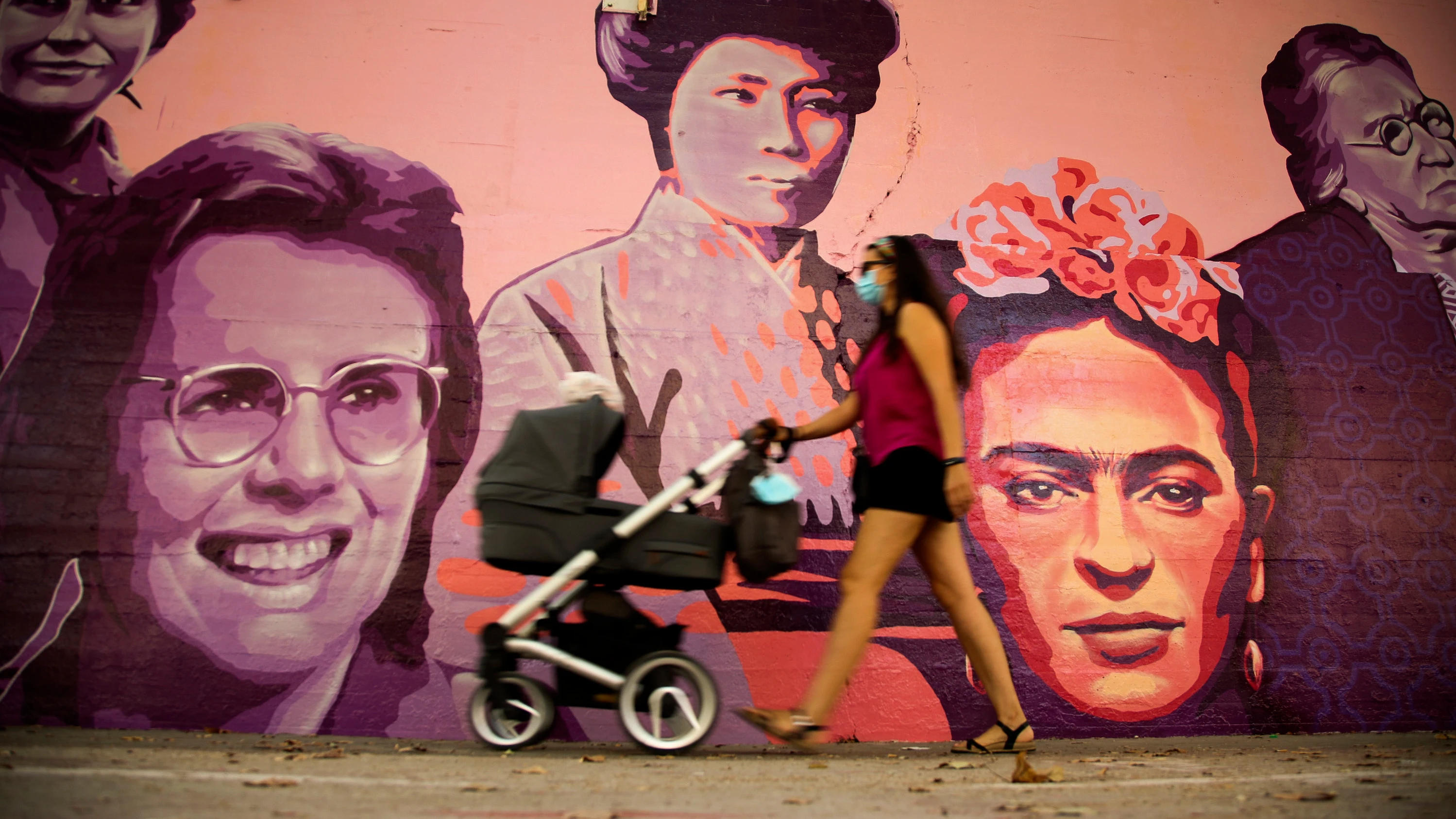 Una mujer camina junto al mural de las mujeres del barrio de Ciudad Lineal en Madrid