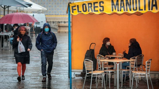 Dos personas en la terraza de un bar protegidas de la lluvia por un toldo de un puesto de flores Lluvia