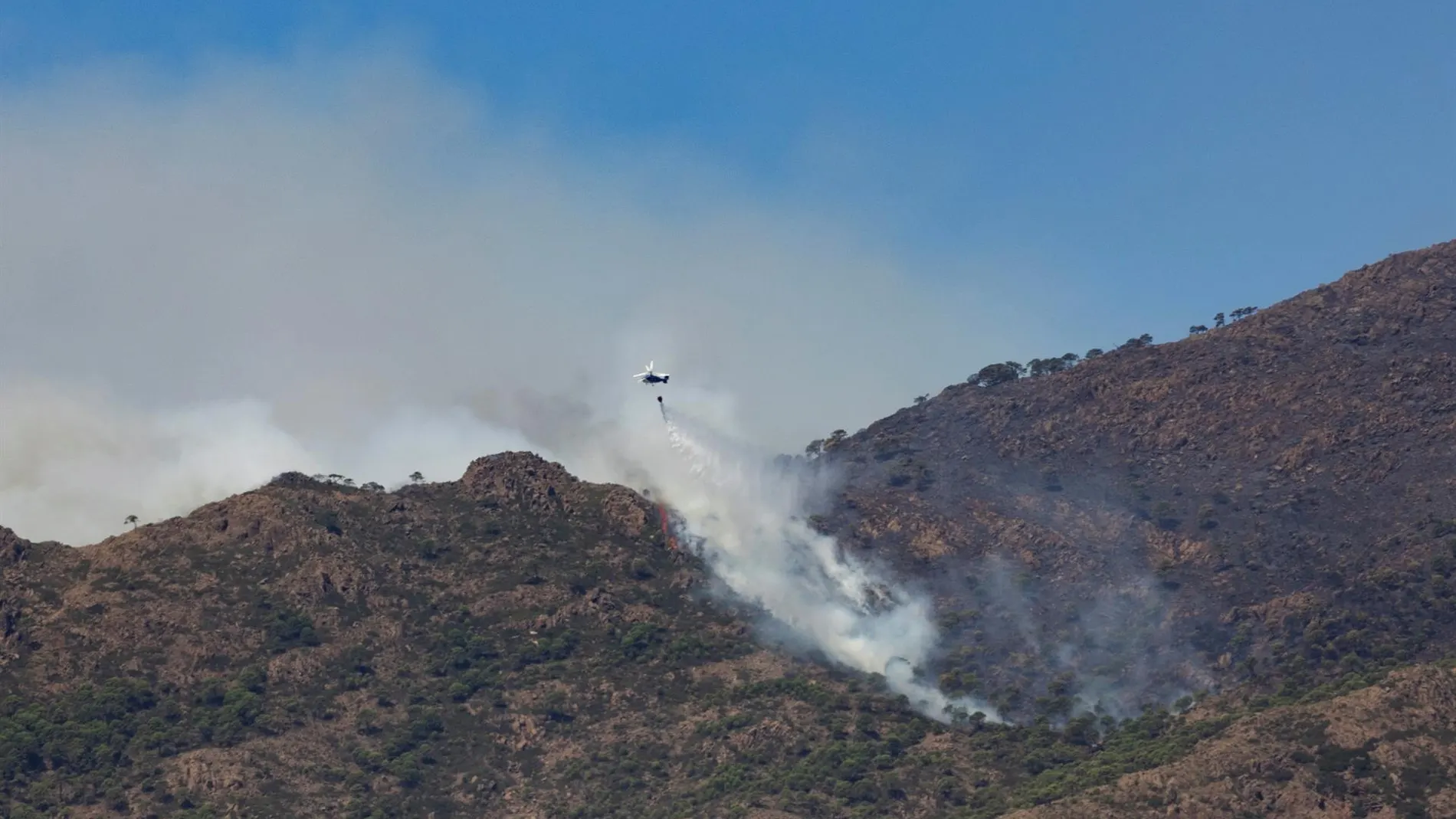  Un helicóptero realiza una descarga en una zona afectada por el incendio de Sierra Bermeja.