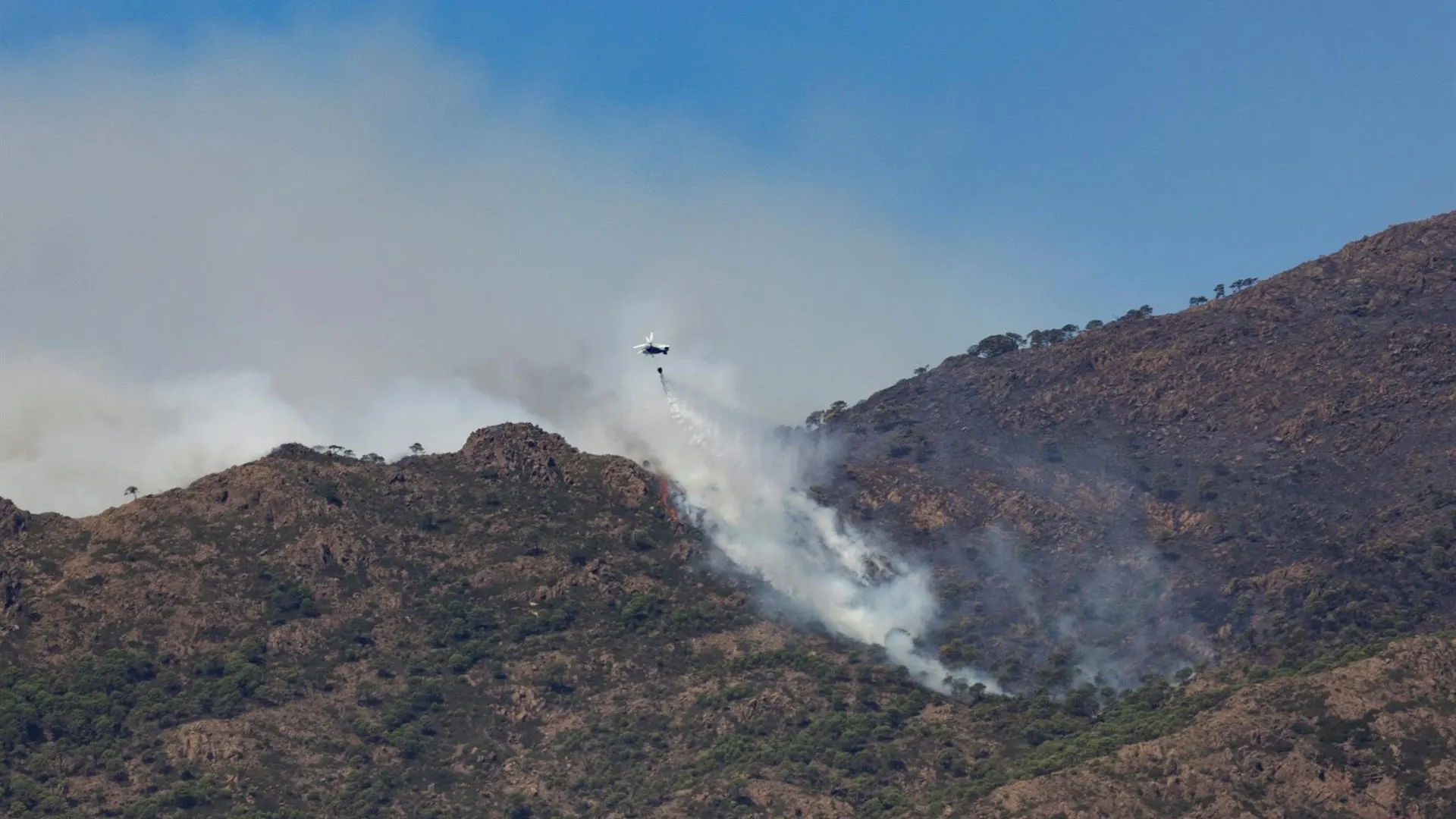  Un helicóptero realiza una descarga en una zona afectada por el incendio de Sierra Bermeja.