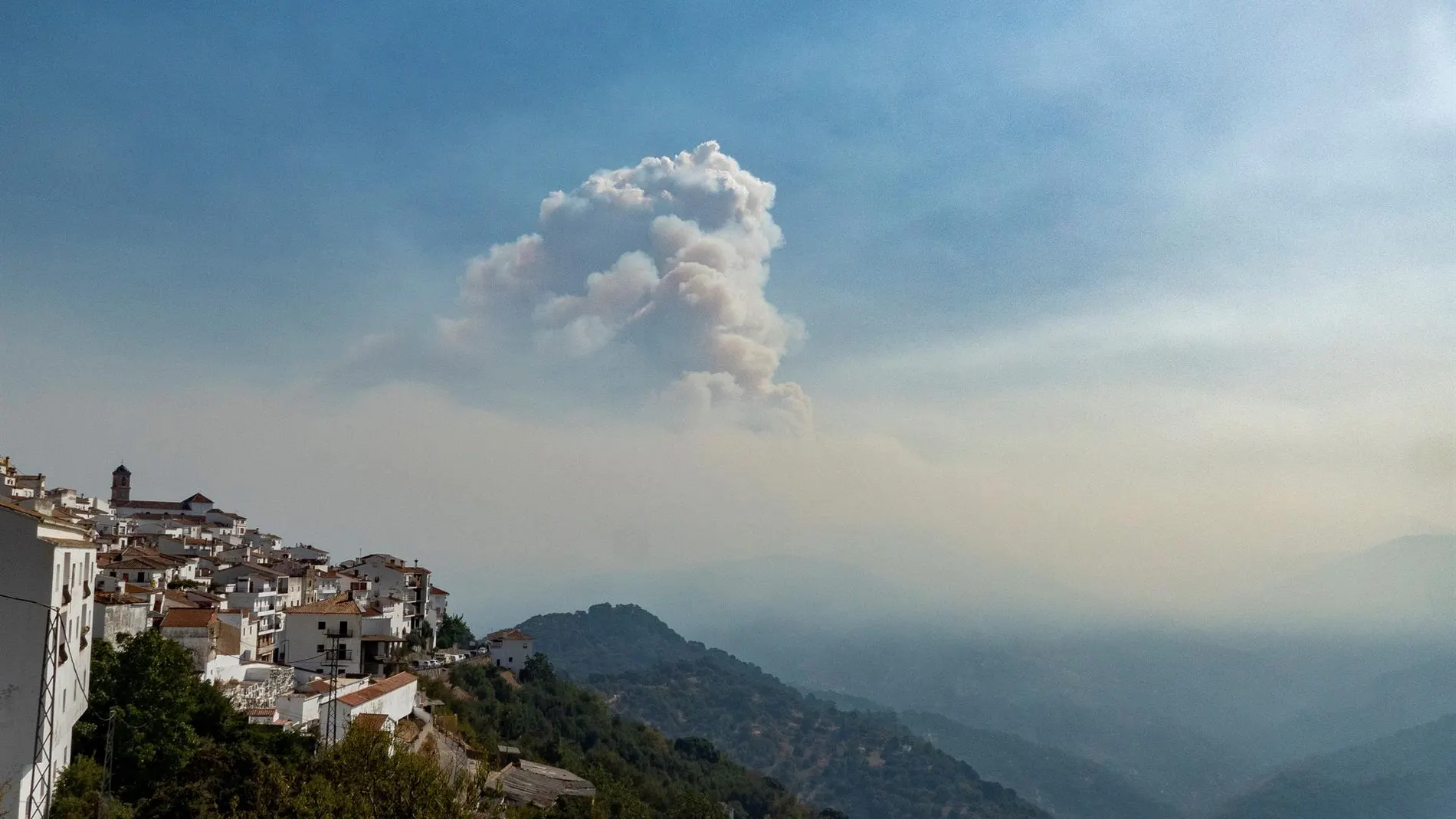 Vista del pueblo de Algatocín junto a una nube de humo que proviene del incendio