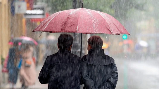 Imagen de dos personas protegiéndose de la lluvia con un paraguas Imagen de dos personas protegiéndose de la lluvia con un paraguas