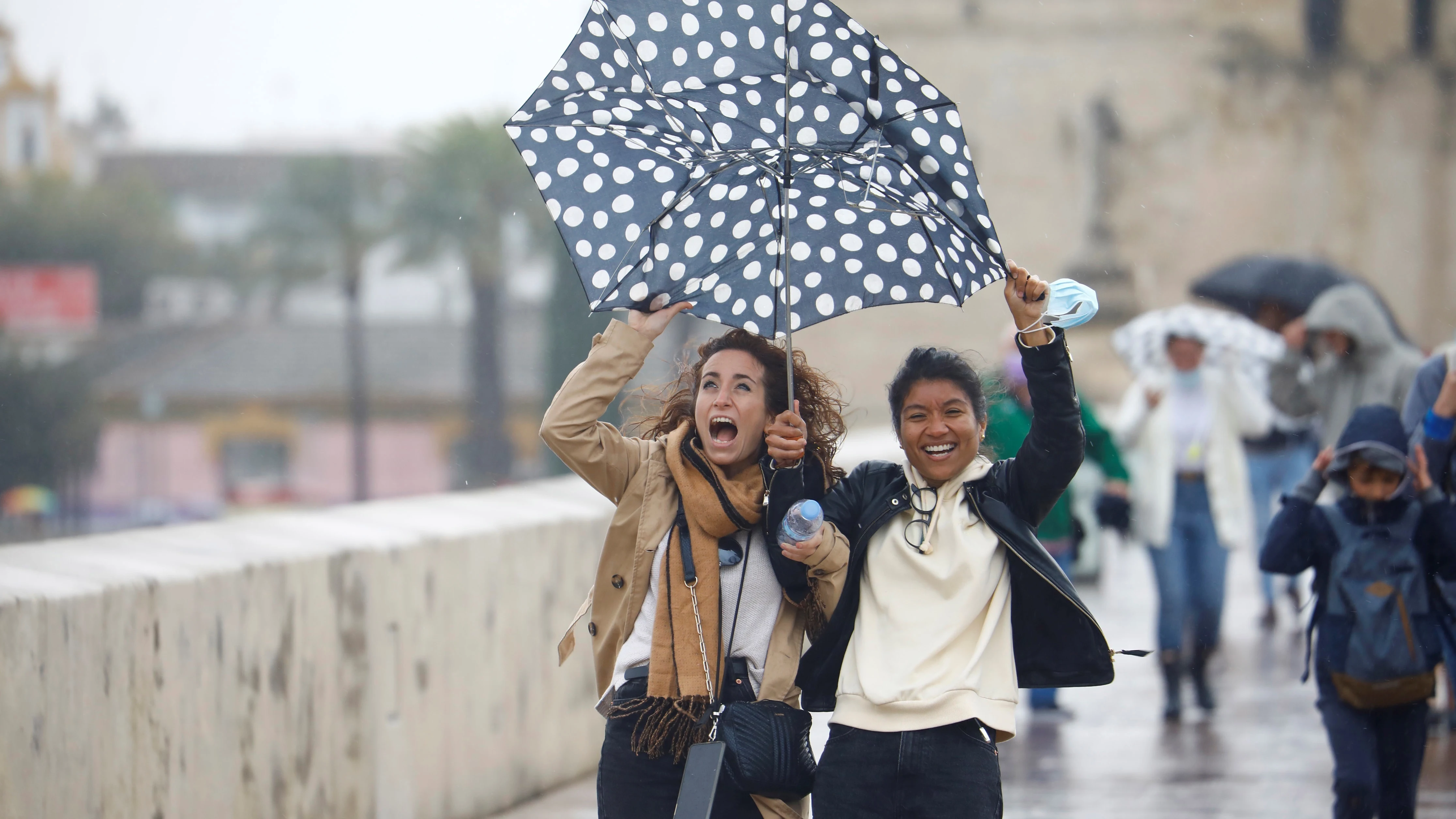 Unas turistas intentan protegerse del viento y de la lluvia con un paraguas mientras caminan por el puente romano de Córdoba