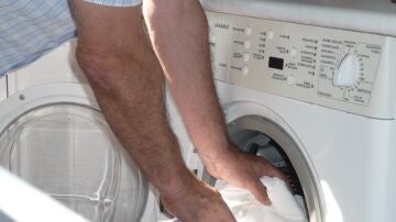 Un hombre introduce ropa en una lavadora doméstica en una foto de archivo