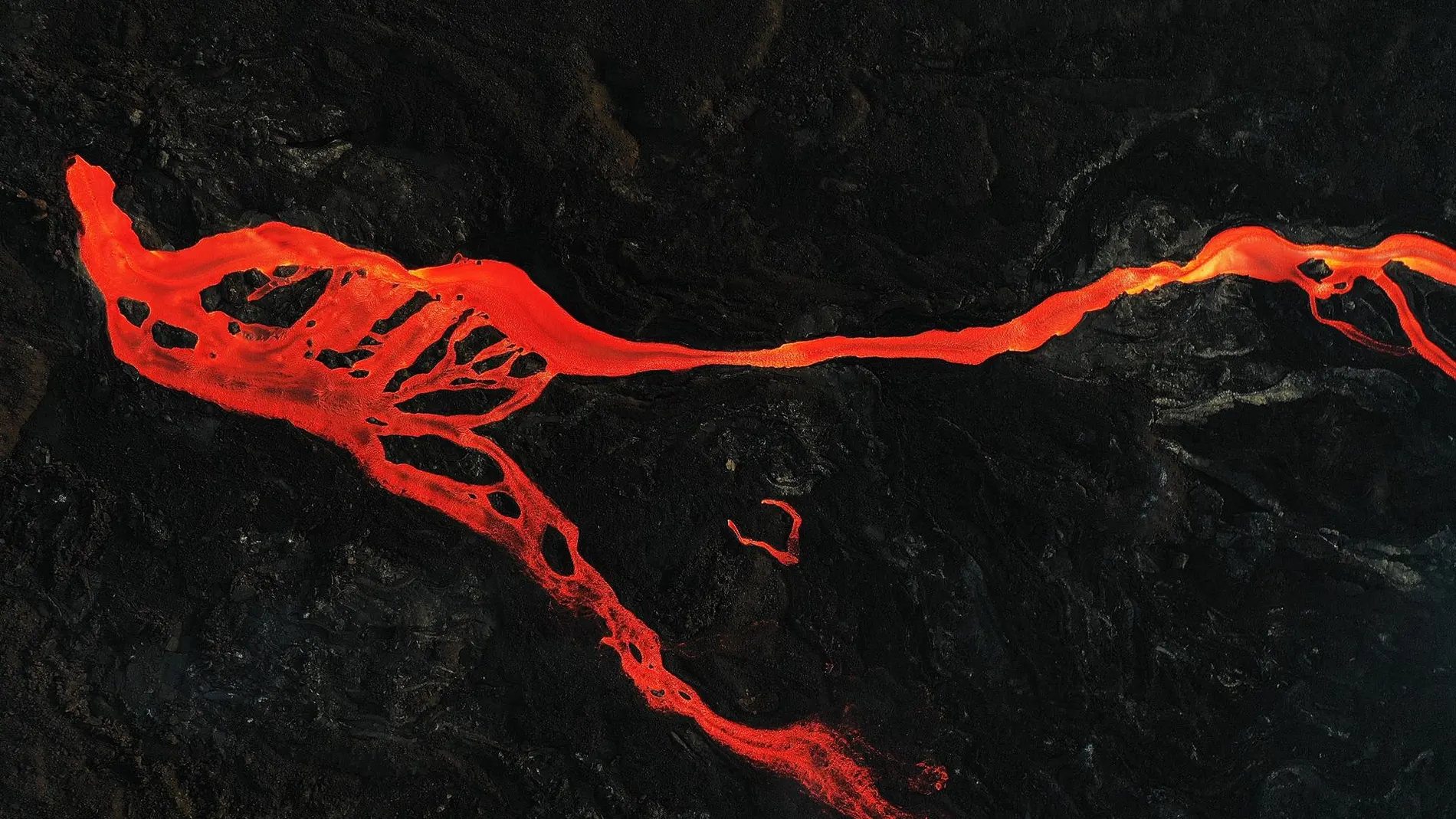 magen tomada con un dron de una colada de magma que discurre hacia el mar rodeada de roca volcánica por la erupción del volcán Cumbre Vieja