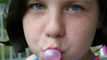 Una niña haciendo una pompa con un chicle
