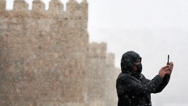 Un hombre se hace una foto con su teléfono móvil junto a la muralla de Ávila durante la primera nevada del otoño en la capital abulense. 