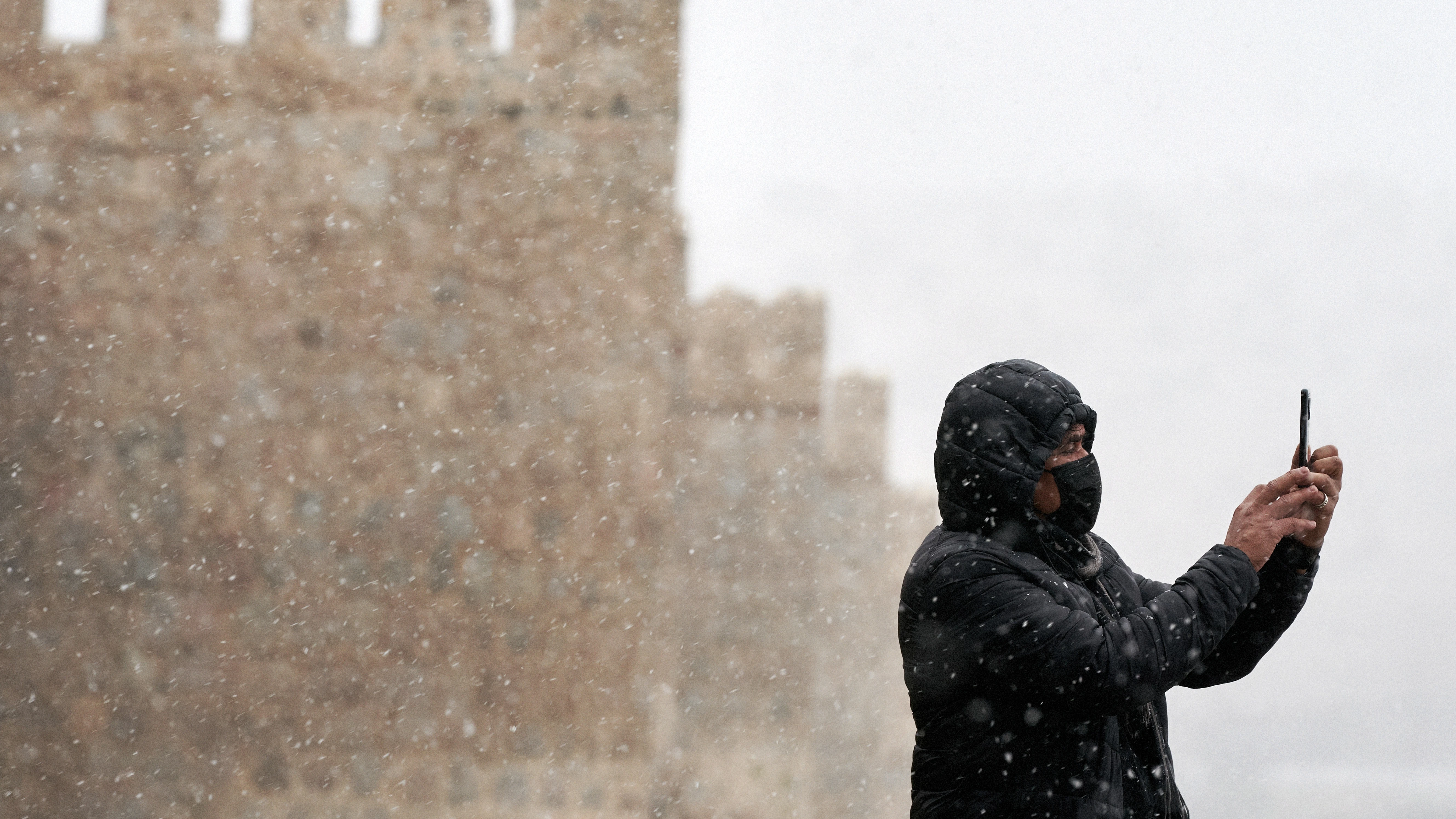 Un hombre se hace una foto con su teléfono móvil junto a la muralla de Ávila durante la primera nevada del otoño en la capital abulense. 