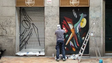Un grafitero decorando la persiana de una tienda