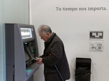 Un hombre de avanzada edad saca dinero de un calero automático de una entidad bancaria. 