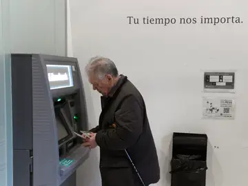 Un hombre de avanzada edad saca dinero de un calero automático de una entidad bancaria. 