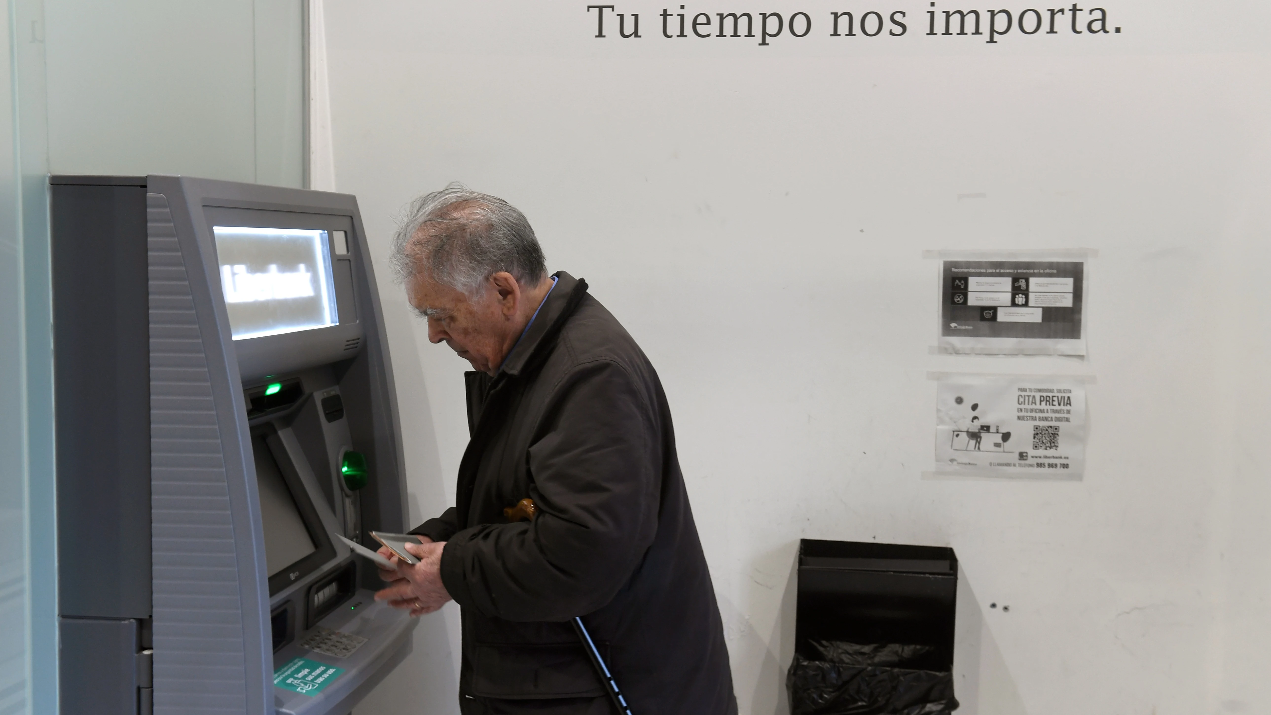 Un hombre de avanzada edad saca dinero de un calero automático de una entidad bancaria. 