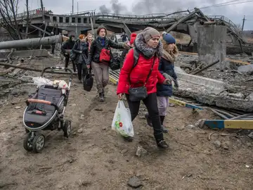 Los civiles cruzan entre los escombros de un puente dañado en la ciudad de Irpín cerca de Kiev