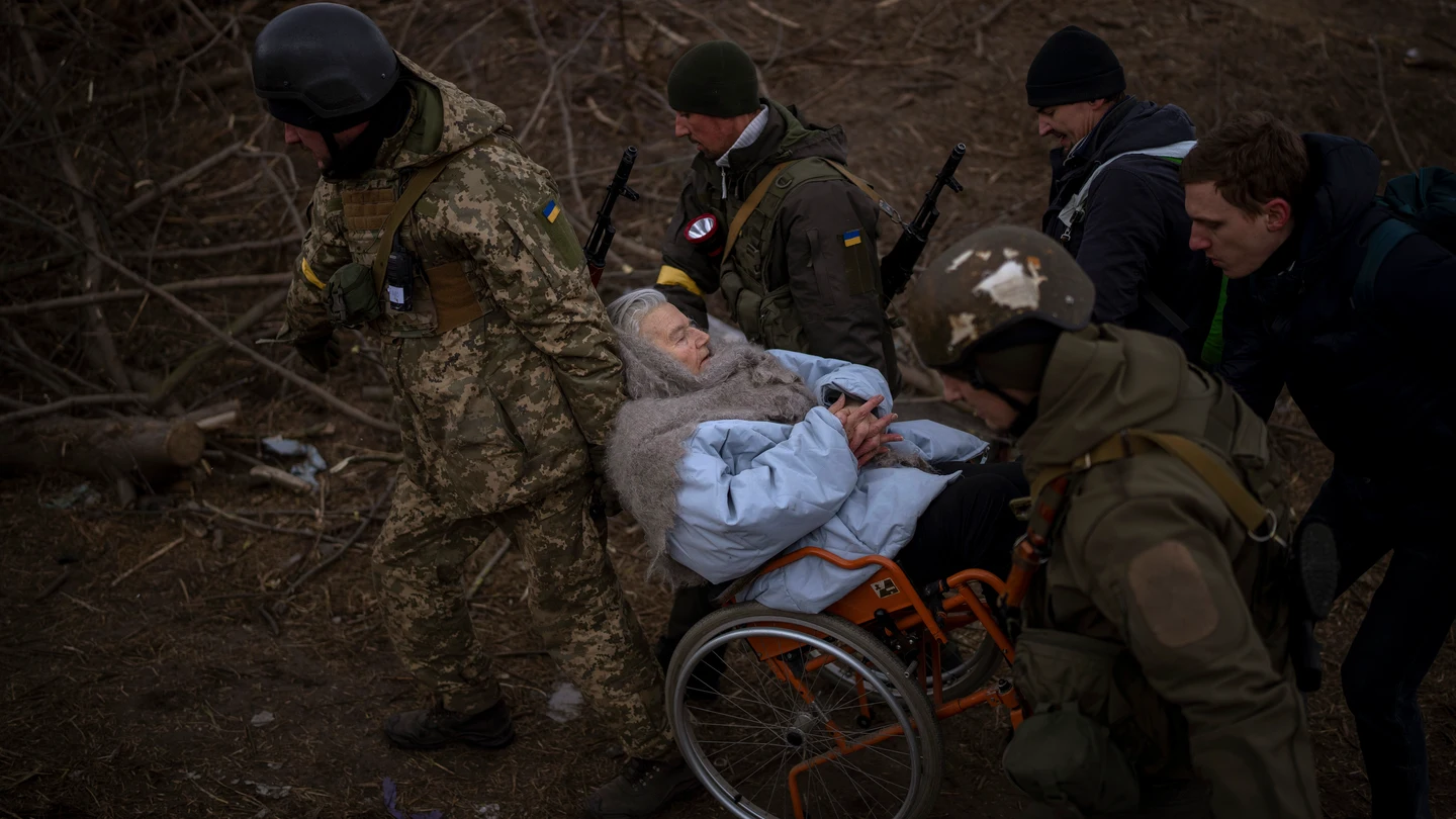 Soldados y milicianos ucranianos cargan a una mujer en silla de ruedas mientras la artillería resuena cerca, mientras la gente huye de Irpin en las afueras de Kiev, Ucrania. Soldados y milicianos ucranianos cargan a una mujer en silla de ruedas mientras la artillería resuena cerca, mientras la gente huye de Irpin en las afueras de Kiev, Ucrania.