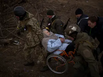 Soldados y milicianos ucranianos cargan a una mujer en silla de ruedas mientras la artillería resuena cerca, mientras la gente huye de Irpin en las afueras de Kiev, Ucrania.