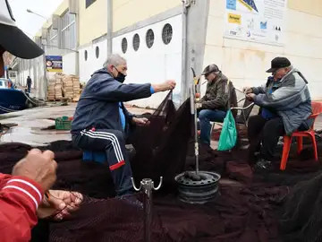 Varios pescadores arreglan los aparejos en el puerto de Almería mientras se desarrolla una manifestación de la flota de los puertos pesqueros 