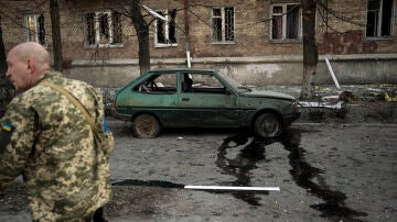 Un soldado ucraniano camina cerca de un automóvil y apartamentos dañados por los bombardeos, en Kiev, Ucrania