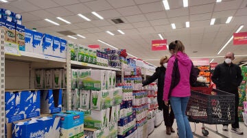 Varias personas compran leche en un supermercado de Madrid, donde algunas estanterías permanecen vacías a causa de la huelga indefinida de transporte