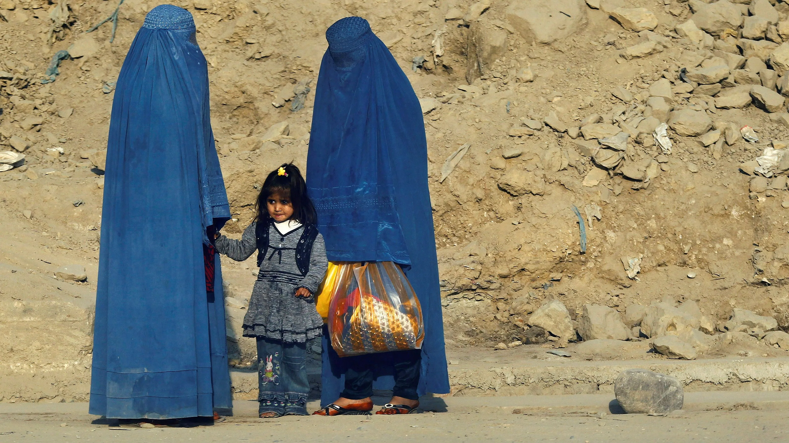  Mujeres afganas vestidas con burkas esperan transporte en una carretera en Kabul