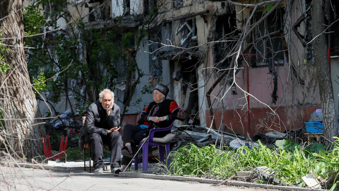 Dos personas sentadas frente a un edificio en ruinas por los ataques rusos en Mariúpol Dos personas sentadas frente a un edificio en ruinas por los ataques rusos en Mariúpol