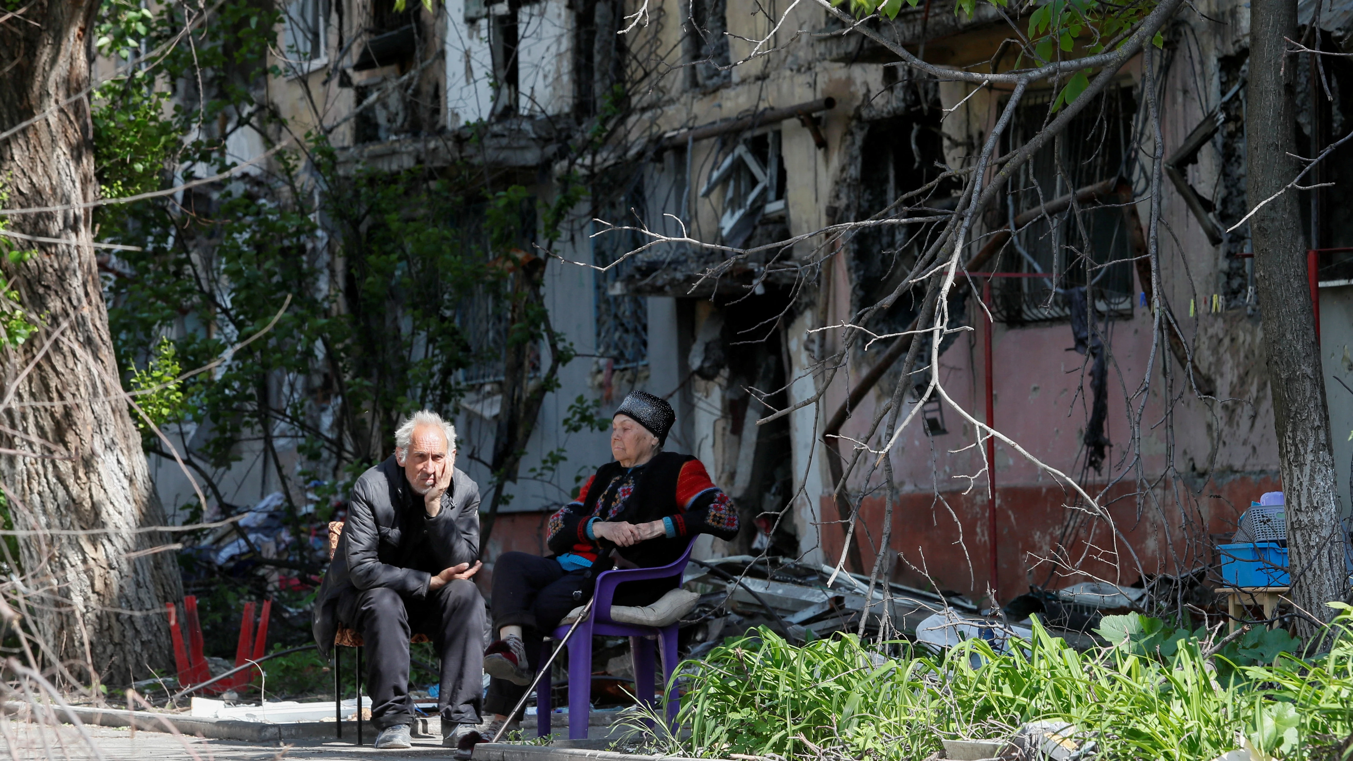 Dos personas sentadas frente a un edificio en ruinas por los ataques rusos en Mariúpol Dos personas sentadas frente a un edificio en ruinas por los ataques rusos en Mariúpol