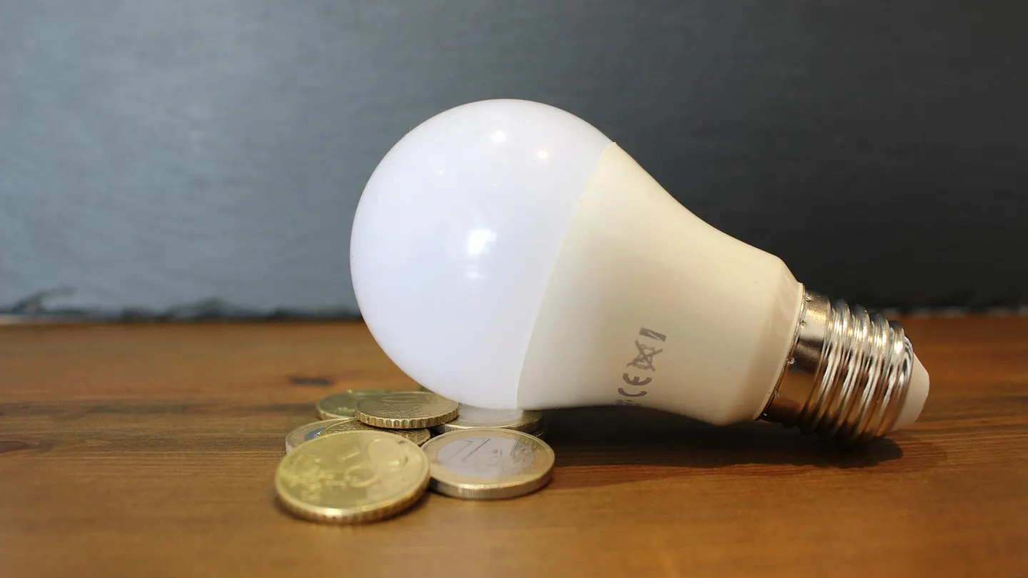 Imagen de una bombillas junto a unas monedas ¿Cuánto va a bajar el precio de la luz con el nuevo tope del gas?