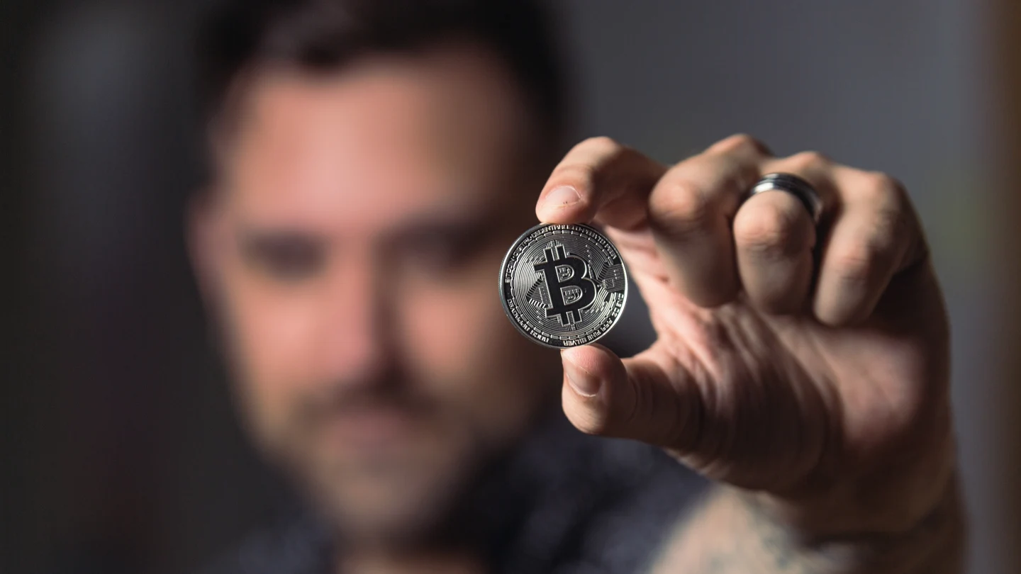 Un hombre sostiene una moneda ilustrando el Boitcoin. Un hombre sostiene una moneda ilustrando el Boitcoin.