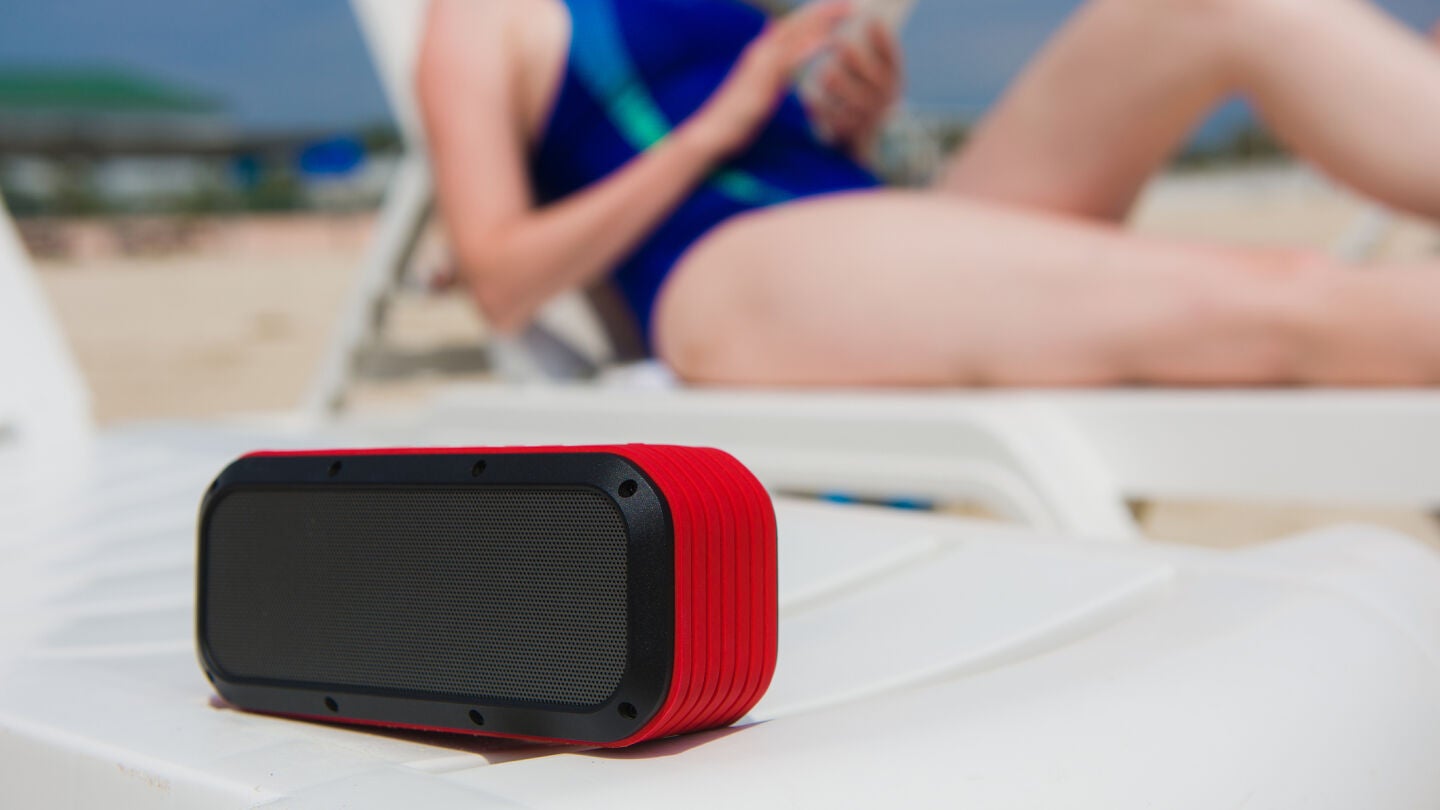 Chica en la playa escuchando m&uacute;sica con un altavoz