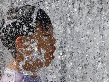 Una persona se refresca en una fuente frente al calor