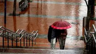 Dos personas pasean protegiéndose de la lluvia.