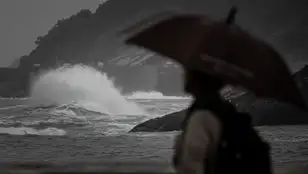 Una persona sostiene un parahuas ante un mar embravecido 