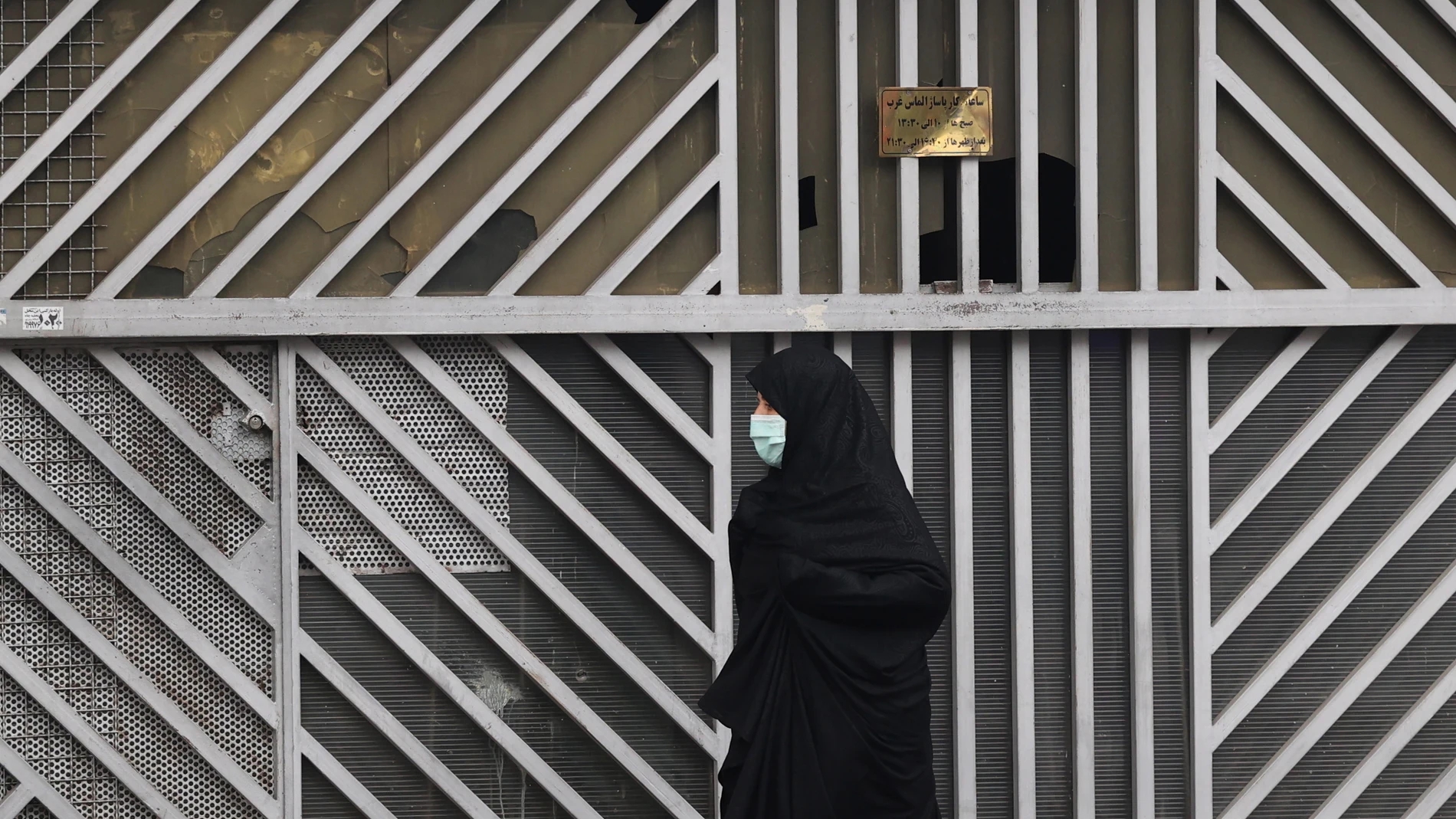 Una mujer con velo camina frente a una tienda cerrada en Teherán.