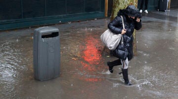 Una mujer corre para protegerse de la lluvia que se registra este martes en Madrid.
