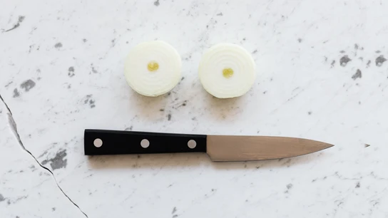 Un cuchillo junto a dos trozos de cebolla cortada Un cuchillo junto a dos trozos de cebolla cortada