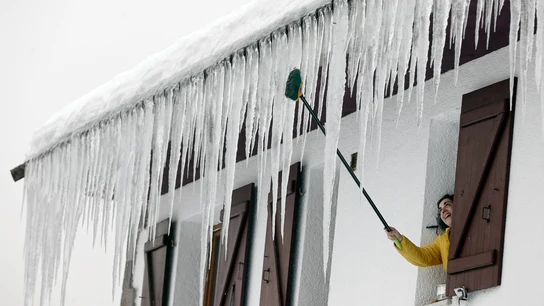Una persona abre la ventana de su casa donde grandes carámbanos de hielo penden del tejado Una persona abre la ventana de su casa donde grandes carámbanos de hielo penden del tejado