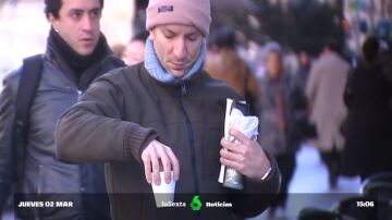 Un joven sujeta un café muy caliente mientras camina por la calle