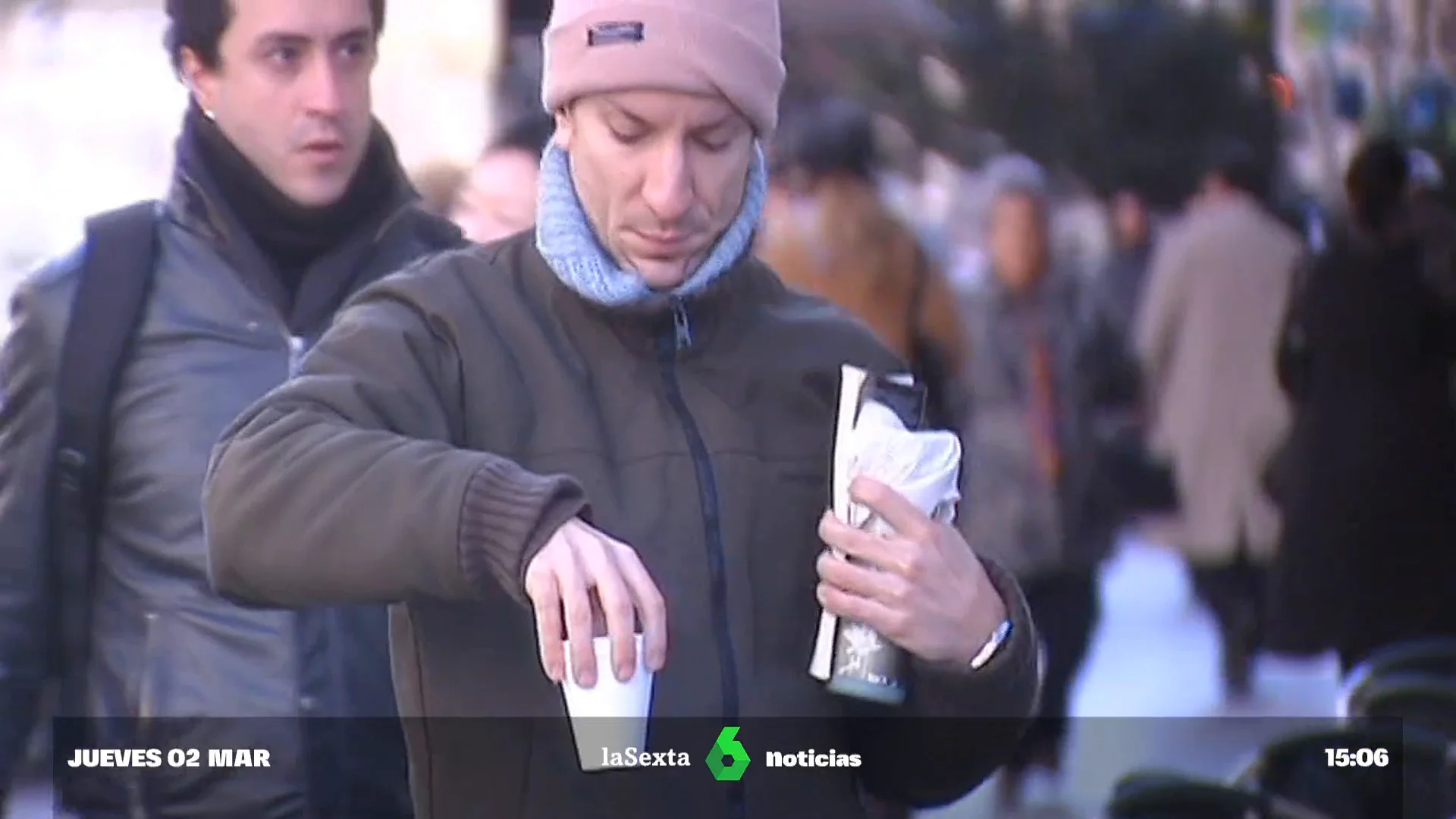 Un joven sujeta un café muy caliente mientras camina por la calle