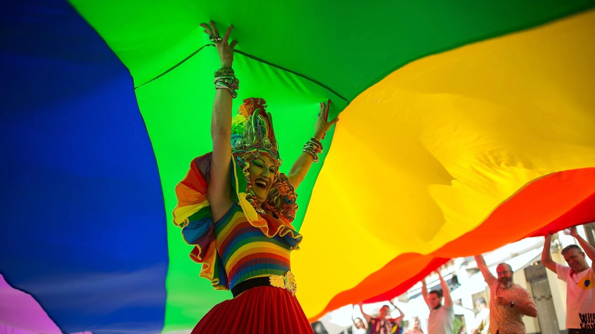 Un drag bajo una bandera LGTBIQ+ gigante durante el desfile del Orgullo LGTBIQ en Málaga.
